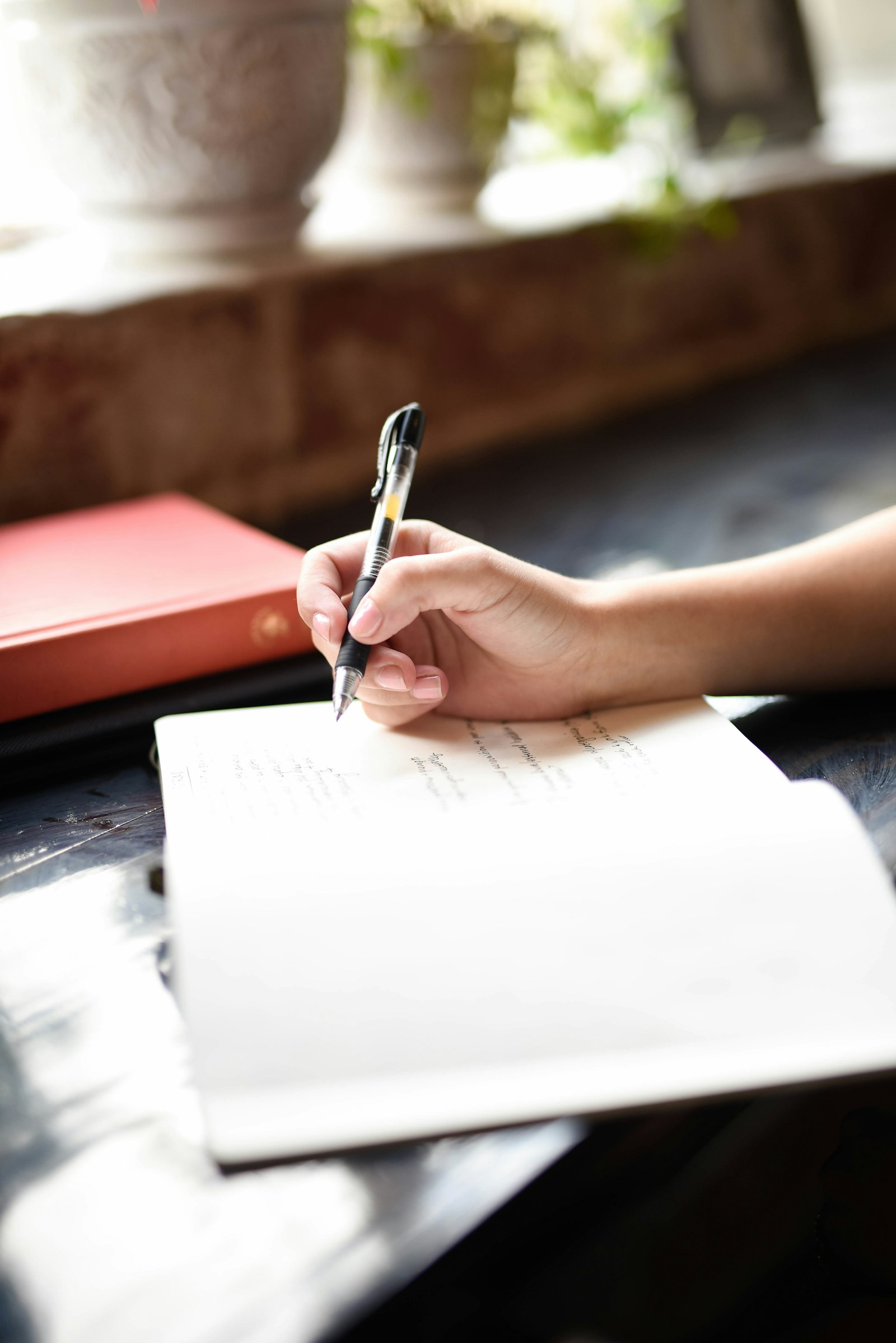 Main qui écrit au stylo dans un carnet ouvert posé sur une table en bois