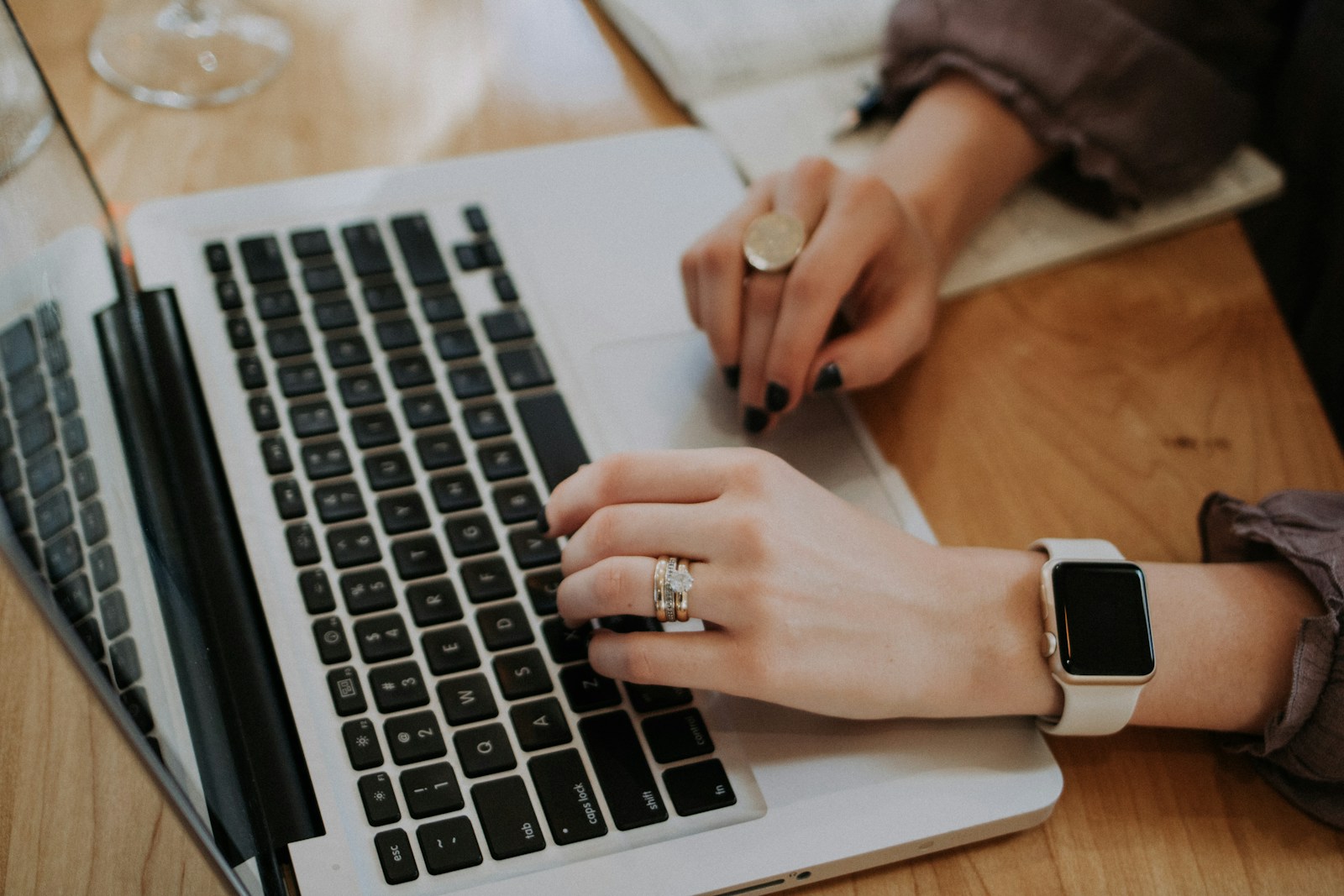Mains d'une personne qui tape sur le clavier d'un ordinateur portable posé sur un bureau en bois